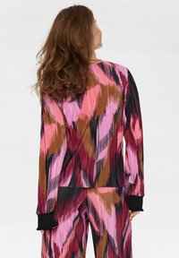 Dažādu krāsu plīsuša apģērba komplekts rozā, melnā un brūnā krāsā ar garām piedurknēm un ribotām aprocēm. Raksts ietver vertikālas svītras un abstraktas formas.