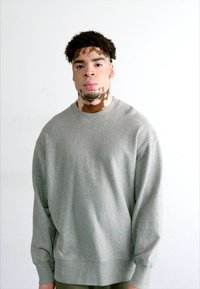 Sudadera gris de manga larga con puños acanalados y cuello redondo. Cuenta con una textura suave y un ajuste relajado, combinada con pantalones verde oliva.