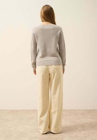 Pull en tricot gris avec un motif texturé, associé à un pantalon en velours côtelé beige à jambes larges. Le pull présente un col rond et des poignets côtelés.