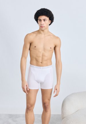 Λευκά βαμβακερά μποξεράκια με λογότυπο στη λάστιχη μέση. Λεία υφή, εφαρμοστή γραμμή και μήκος πάνω από το γόνατο. Το μοντέλο απεικονίζεται χωρίς πουκάμισο.