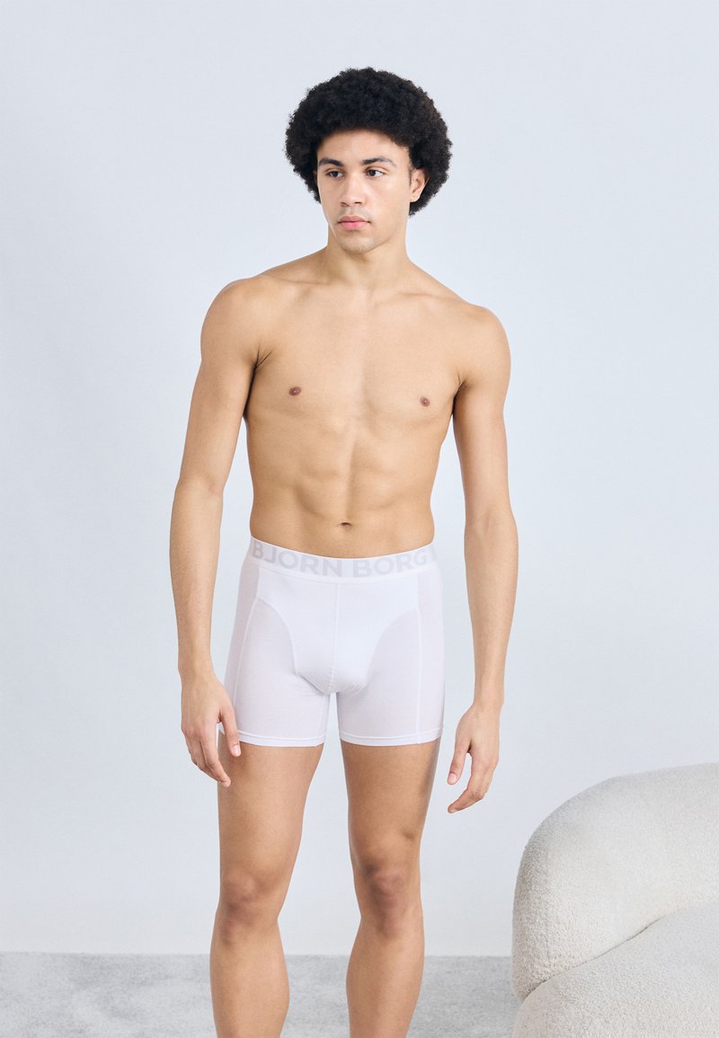 Λευκά βαμβακερά μποξεράκια με λογότυπο στη λάστιχη μέση. Λεία υφή, εφαρμοστή γραμμή και μήκος πάνω από το γόνατο. Το μοντέλο απεικονίζεται χωρίς πουκάμισο.