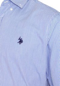 Camicia a righe blu e bianche con colletto e logo del giocatore di polo ricamato in blu navy sul petto.
