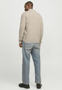 Beige geripptes Sweatshirt mit hohem Kragen, getragen über hellblauen lockeren Jeans, präsentiert dunkle Stiefel und ein einfaches Design.