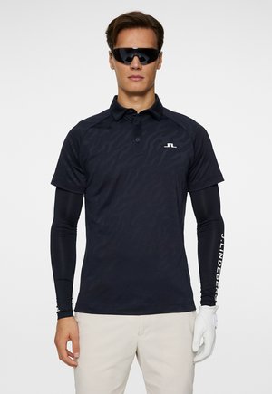 Navy polo shirt with subtle pattern, short sleeves, and collar. Worn with black long sleeves and golf glove. Reflective sunglasses.