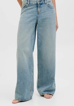 Világoskék, széles szárú farmernadrág, mezítláb viselve, elülső zsebekkel, övhurkokkal és gombos sliccel, egyszínű háttér előtt.