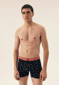 Czarne bokserki z czerwonymi wzorami w serca. Czerwony pas z logo "HENDERSON". Gładki materiał i dopasowany krój. Model pokazuje widok z przodu.