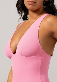 Roze bodysuit met een diepe V-hals en brede bandjes. Gemaakt van een gestructureerd materiaal, met een getailleerd ontwerp dat de vormen benadrukt.