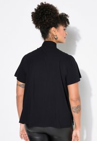 Top nero a maniche corte con collo alto, caratterizzato da un design fluido e una texture morbida. Fessure laterali evidenti sull'orlo.