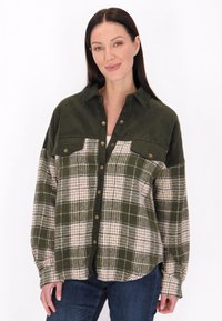 Camisa a cuadros verde y crema con cuello de botón, dos bolsillos en el pecho y textura de pana. Presenta botones de presión dorados y mangas largas.