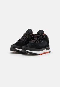 Paire de baskets de sport noires avec des détails orange et blancs, semelles épaisses et lacets noirs, placées côte à côte sur un fond uni.