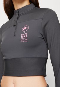 Nike kortärmad svart långärmad topp med halvdragkedja, ribbad struktur och rosa tryckt logotyp och text framtill.