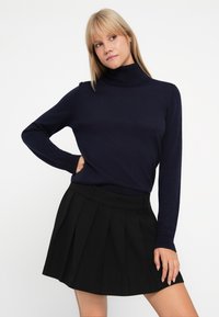 Navy turtleneck sweater in a fitted design, paired with a pleated black skirt. The sweater has long sleeves and a smooth texture.