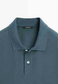 Polo bleu-vert texturé avec un col côtelé, deux boutons blancs, et une étiquette Massimo Dutti à l'intérieur du col.