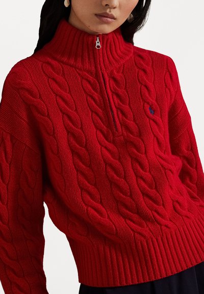 Red cable-knit pullover with a high collar and half-zip front. Ribbed cuffs and hem, featuring a small embroidered logo on the chest.