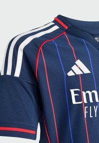 Maglia da calcio navy con strisce bianche sulle spalle, linee verticali rosse e blu, colletto a coste e il logo bianco "Emirates Fly" in evidenza.