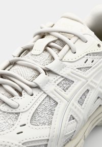 Valge spordijalats, millel on tekstureeritud võrgust ülaosa, sujuvad pealsed ja paelad. Tugevdatud silmused ja pehmendusega tald, mis on minimalistliku disainiga.