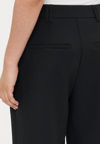 Black tailored trousers with a smooth fabric, featuring a high waistband, two back pockets, and subtle stitching details.
