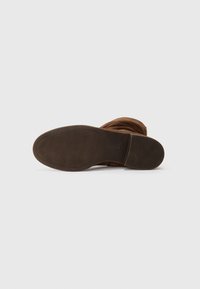 Stivale alla caviglia in suede marrone con una suola in gomma testurizzata e materiale morbido e arricciato nella parte superiore. Punta liscia e arrotondata con dettagli minimi.