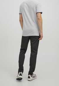 Grå pikétröja med svart kant, kombinerad med mörkgrå slim-fit-byxor och flersfärgade sneakers. Vy från baksidan, enfärgad bakgrund.