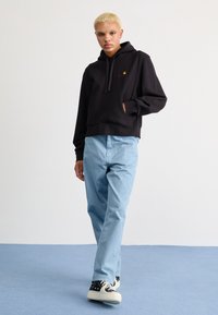 Black cropped hoodie with a kangaroo pocket and red logo detail, paired with light blue straight-leg pants and black and white sneakers.