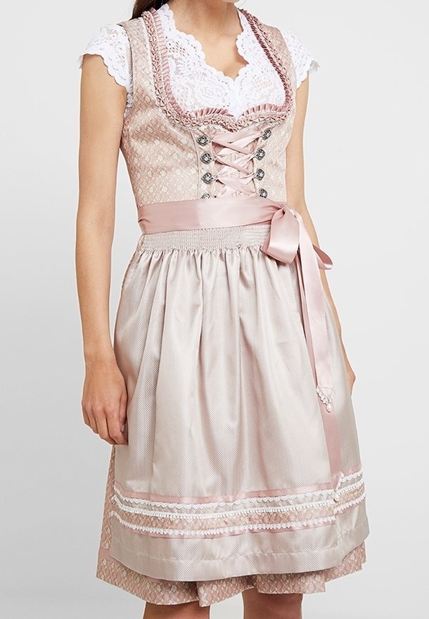 Femme portant une robe traditionnelle dirndl rose pastel avec corsage à lacets, blouse blanche en dentelle et tablier en satin noué à la taille.