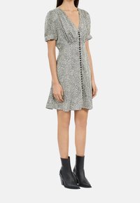 Sukienka w wzór lamparta w czerni i bieli, z krótkimi bufiastymi rękawami, dekoltem w serek oraz zapięciem na guziki z przodu. Stylizowana z czarnymi botkami do kostek.