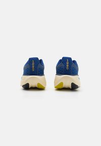 Baskets de course en maille bleu marine, avec un dessus texturé, des accents jaunes et une semelle rembourrée dotée d'éléments de traction noirs et jaunes.