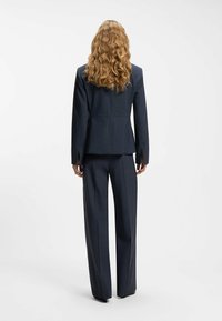 Abito su misura blu scuro con blazer strutturato e pantaloni a gamba dritta. Presenta una texture liscia del tessuto e un delicato motivo a righe sottili.