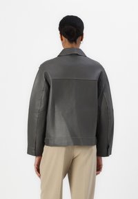 Grau Lederjacke mit lässiger Passform, sichtbaren Nähten und klassischem Kragen. Verfügt über ein schlichtes Design und eine glatte Textur.