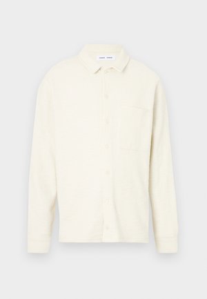 Krém színű gombos ing, texturált anyagból, gallérral és egyetlen mellzsebbel. Hosszú ujjú és laza szabású. Minimalista dizájn.