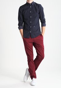 Mörkblå knappar-skjorta med vita prickar, ihop med åtsittande bourgognebyxor och vita sneakers. Klassisk krage och långa ärmar.