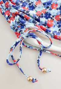Tissu fleuri avec des fleurs bleues, rouges et blanches, doté d'un cordon froncé se terminant par des perles dorées.