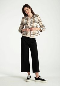 Beige Tweedjacke mit schwarz-orangefarbenem Karomuster, 3/4-Ärmel und Fransenverarbeitung. Kombiniert mit einem hellen Oberteil und schwarzen weitgeschnittenen Hosen.