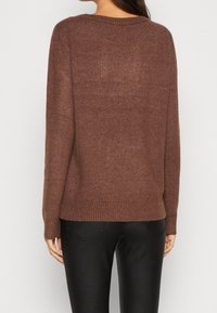 Brun stickad tröja med rundad halsringning, långa ärmar och ribbad nederkant. Mjuk textur, avslappnad passform, lämplig för lager-på-lager.
