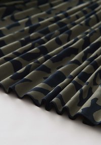 Tissu à motif camouflage en vert olive et bleu marine foncé, présentant des plis et une texture lisse avec un bord ondulé.