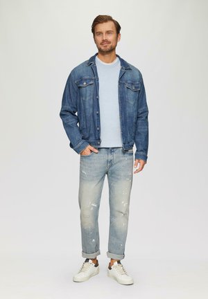Denim jacket met klassiek ontwerp, lichtblauw t-shirt met ronde hals, versleten lichtblauwe spijkerbroek en witte sneakers met donkere accenten.