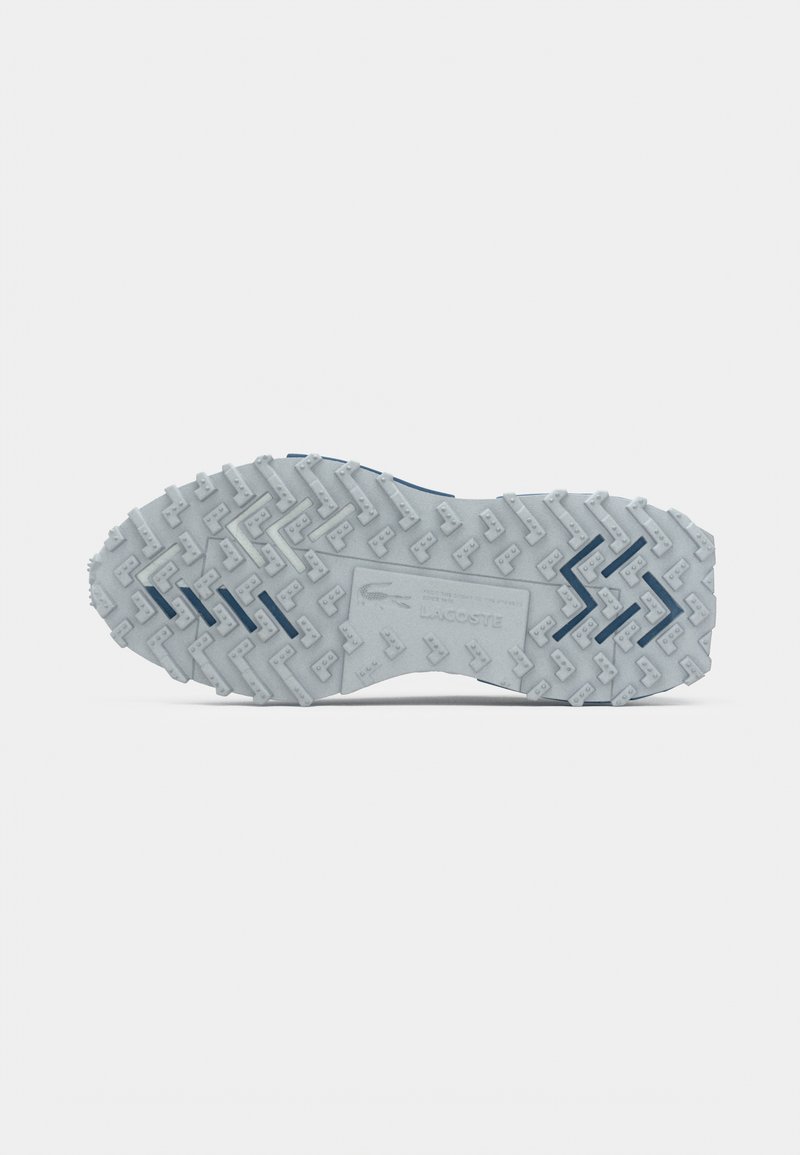 Semelle extérieure en caoutchouc gris avec un motif en zigzag texturé et de petits crampons, comportant un accent bleu près du talon et un logo au centre.