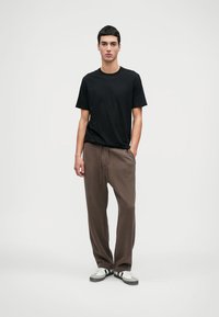 Μαύρο βαμβακερό μπλουζάκι συνδυασμένο με καφέ φόρμες από τζέρσεϊ. Οι φόρμες διαθέτουν ελαστική μέση και πλαϊνές τσέπες. Λευκά και μαύρα αθλητικά παπούτσια.