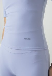Light purple athletic top made from smooth, stretchy fabric featuring short sleeves and a fitted design. "STRONGER" logo near the hem.