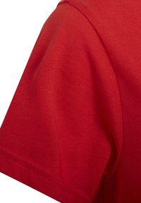 Sarkanais kokvilnas T-krekls ar apaļu kakla izgriezumu un īsām piedurknēm, ar gludu tekstūru un tīru vīlēšanu gar apakšmalu un plecu šuvēm.