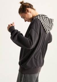 Donkergrijze hoodie gemaakt van zachte stof, met een gestreepte binnenkap en een losse pasvorm met ribboord aan de onderkant en mouwen.