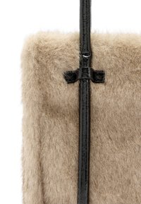 Beżowa futerkowa torebka z eleganckim czarnym paskiem z lakierowanej skóry. Miękka w dotyku o gładkiej powierzchni, ozdobiona prostym węzłem jako detal.