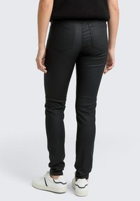 Svarta skinny jeans med en slät, strukturerad yta. Har två bakfickor med en lätt avsmalning och bärs med vita sneakers.