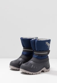 Bottes de neige en tissu bleu avec semelles en caoutchouc gris, doublure en polaire et fermetures à velcro. Présente un motif de dinosaure sur le côté.