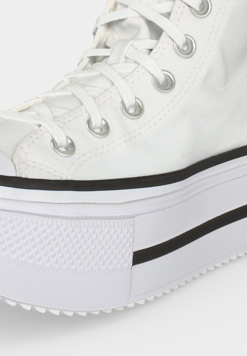 Primo piano di una sneaker alta bianca con occhielli argentati, lacci bianchi e una spessa suola platform bianca con dettaglio di striscia nera.