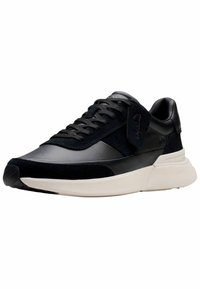 Zapatillas negras que presentan una combinación de materiales de piel y gamuza, con un diseño minimalista, suela intermedia blanca gruesa y cordones negros.