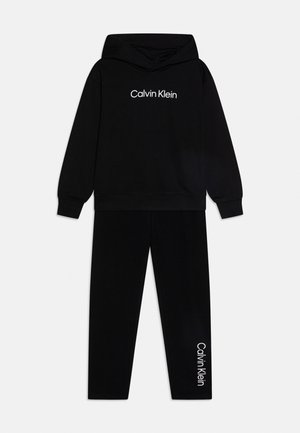 Schwarzes Hoodie- und Jogginghosen-Set mit weißem "Calvin Klein"-Logo auf der Brust und am unteren Bein, flach auf hellem Hintergrund dargestellt.