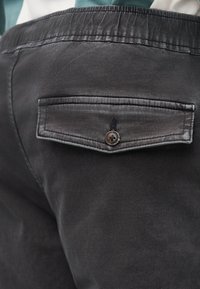 Τα μαύρα τζιν παντελόνια διαθέτουν πίσω τσέπη με κλείσιμο με κουμπί και διακριτικές ραφές. Το ύφασμα έχει λεία, ματ υφή.