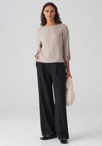 Beige, satinähnliches Oberteil mit quadratischem Ausschnitt und Dreiviertelärmeln, kombiniert mit weit geschnittenen schwarzen Hosen und einer cremefarbenen Kunstfell-Clutch.