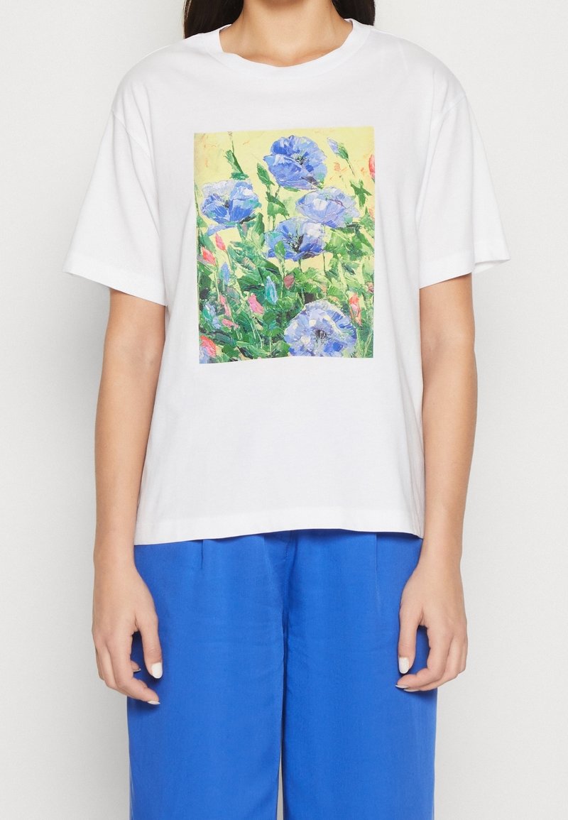 Bílý bavlněný tričko s barevným květinovým potiskem modrých květin na žlutém pozadí. Krátké rukávy a uvolněný střih.